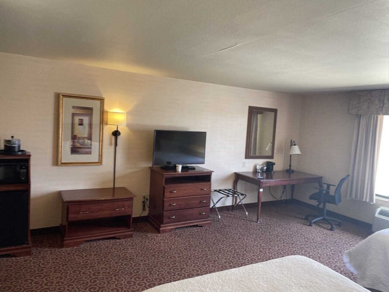 Une chambre d’hôtel comprenant un lit, un bureau avec une chaise, une télévision posée sur une commode et une lampe.