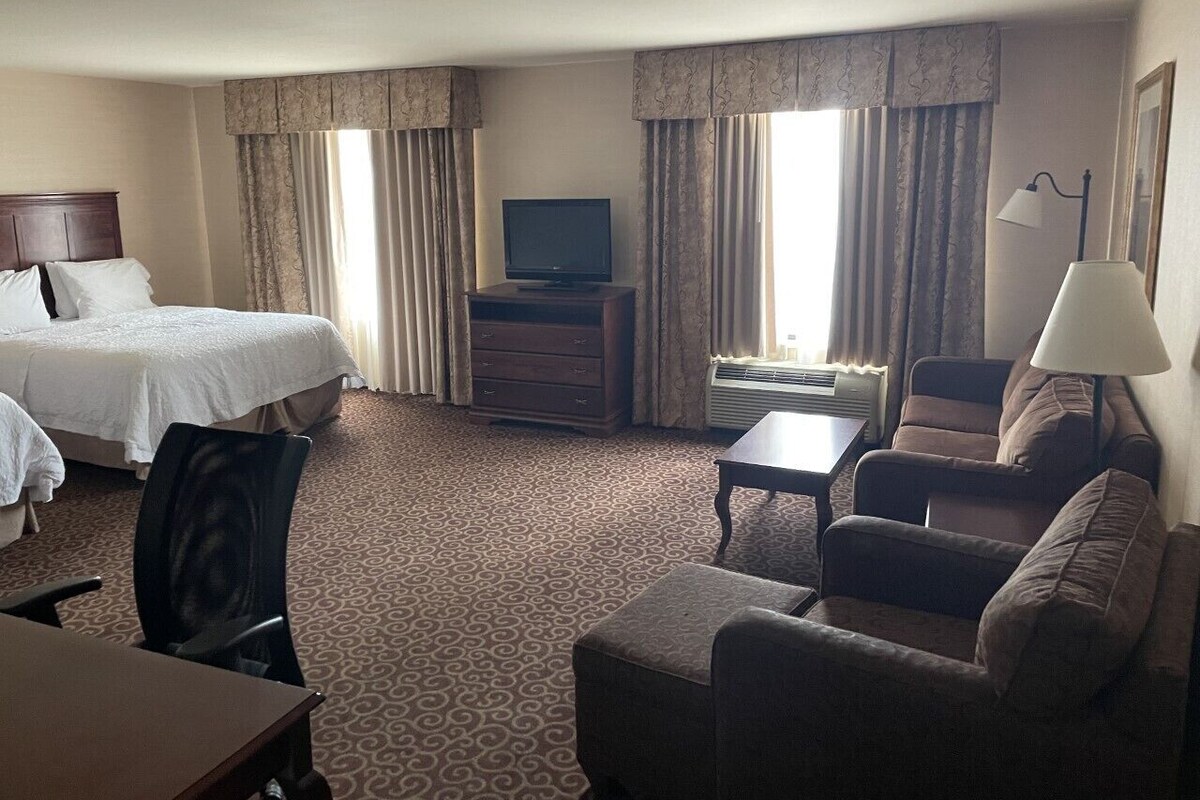 A hotel room with a bed, a desk, a chair, a sofa, a television, and a lamp.