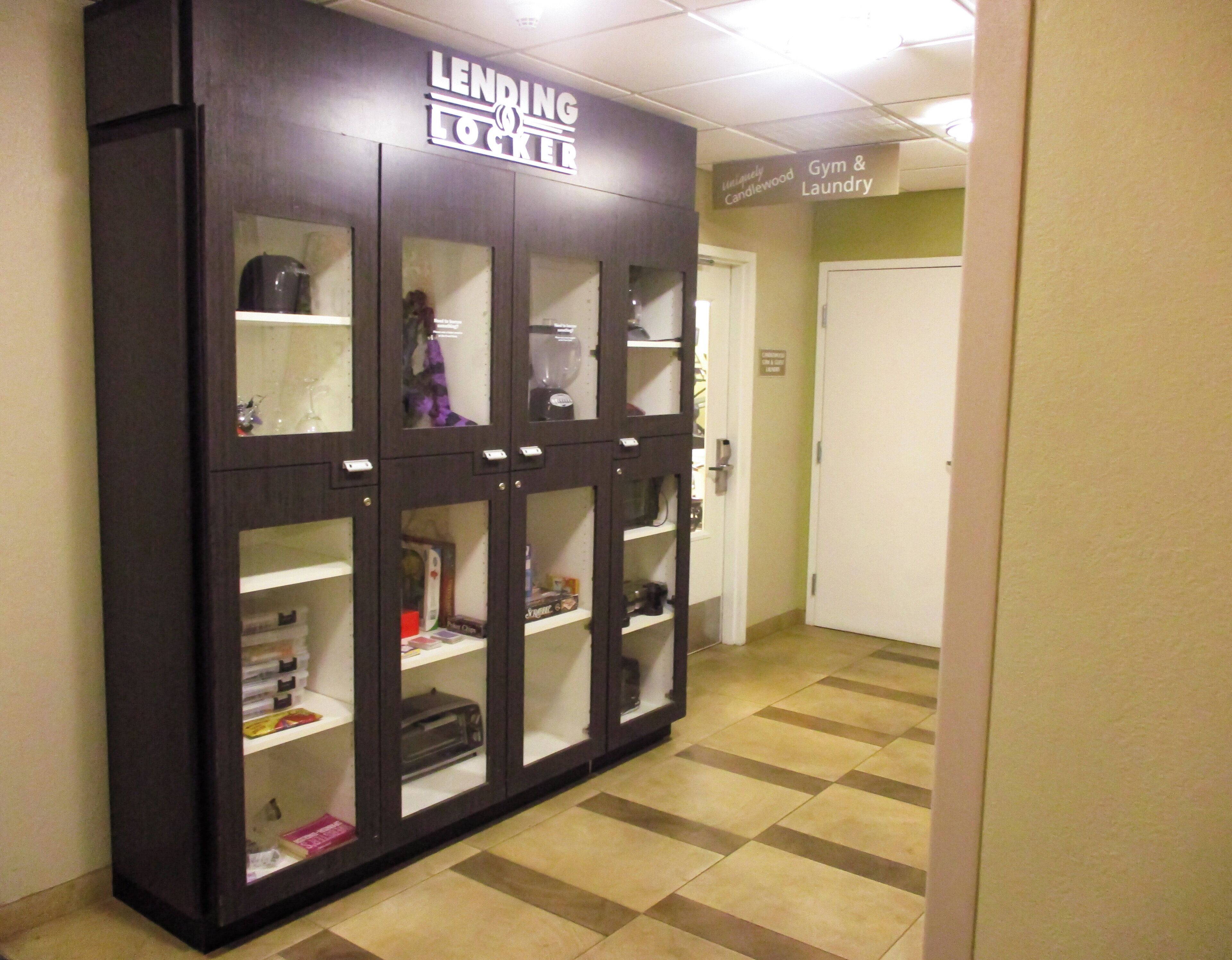 A storage unit labeled 'Lending Locker' with multiple compartments, a door, and a sign indicating 'Gym & Laundry' in the background.