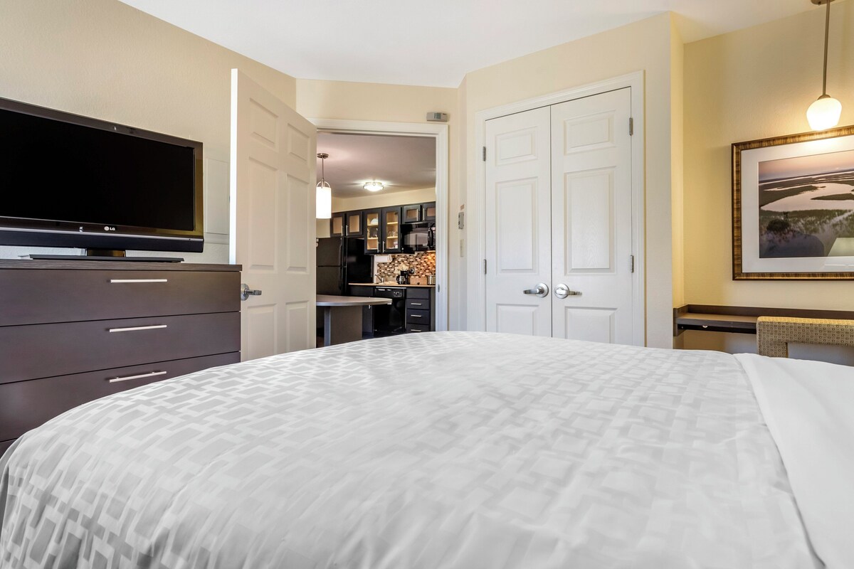 Een slaapkamer met een bed, een televisie, een dressoir en een deur naar een keuken.