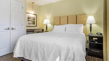 A hotel room with a large bed, two bedside lamps, a desk with a chair, a framed picture on the wall, and a door.