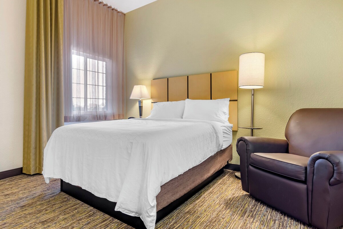 Een hotelkamer met een bed, twee bedlampen, een stoel en een raam met gordijnen.