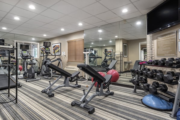 Une salle de sport équipée de tapis de course, d’appareils de musculation et d’un mur entièrement recouvert de miroirs.