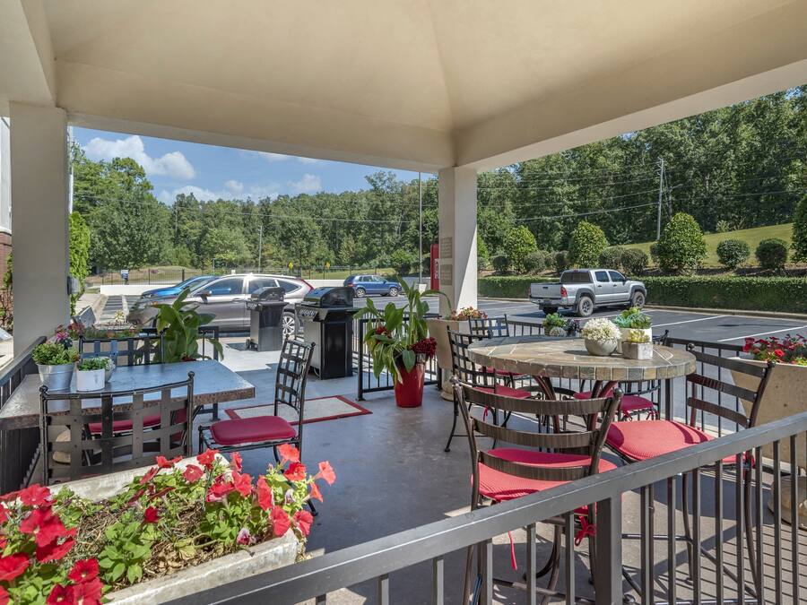 A covered outdoor seating area with tables and chairs, surrounded by potted plants and flowers.
