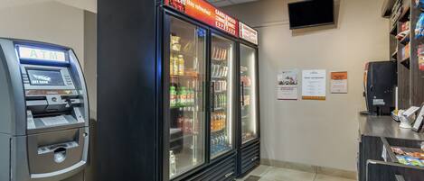 An ATM and a refrigerated display case with beverages and snacks in a store.