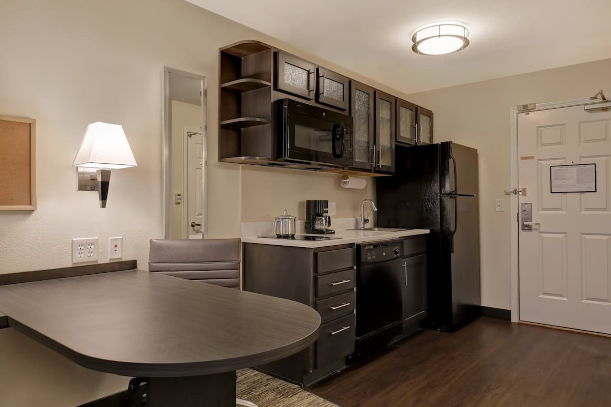 Une cuisine moderne équipée d’un four à micro-ondes, d’une cuisinière et d’un réfrigérateur intégrés, d’une table à manger avec des chaises et d’une lampe fixée au mur.