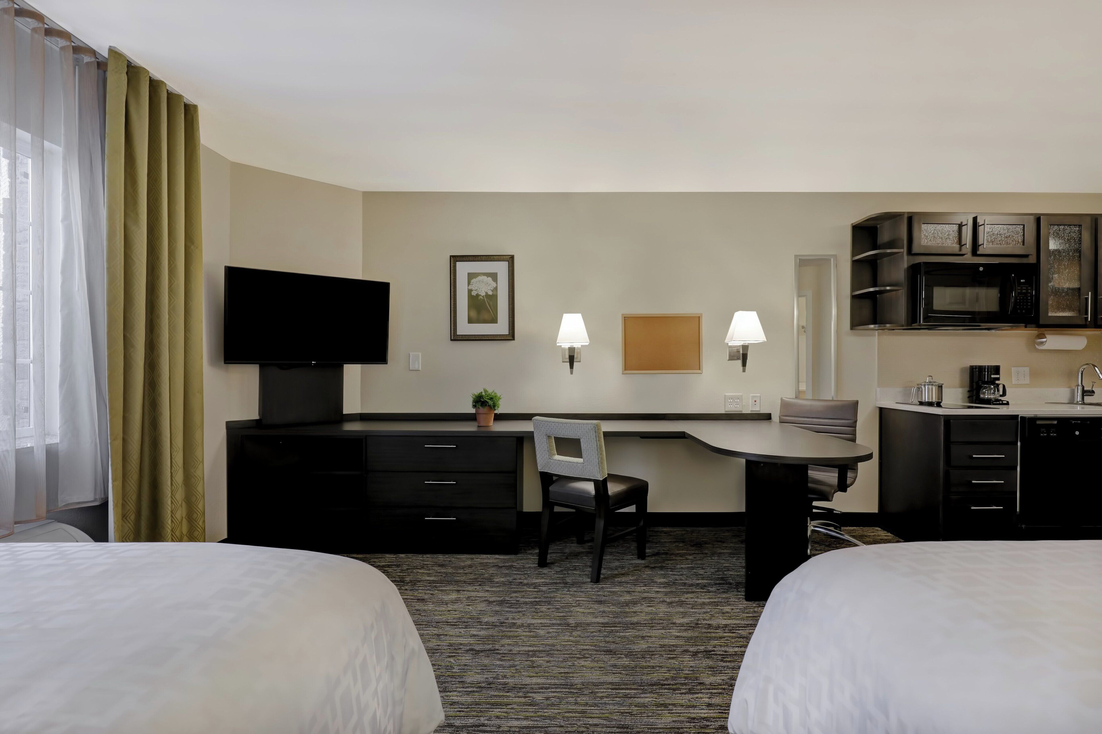 Habitación de hotel con dos camas, un escritorio, un televisor, un microondas y una cafetera.