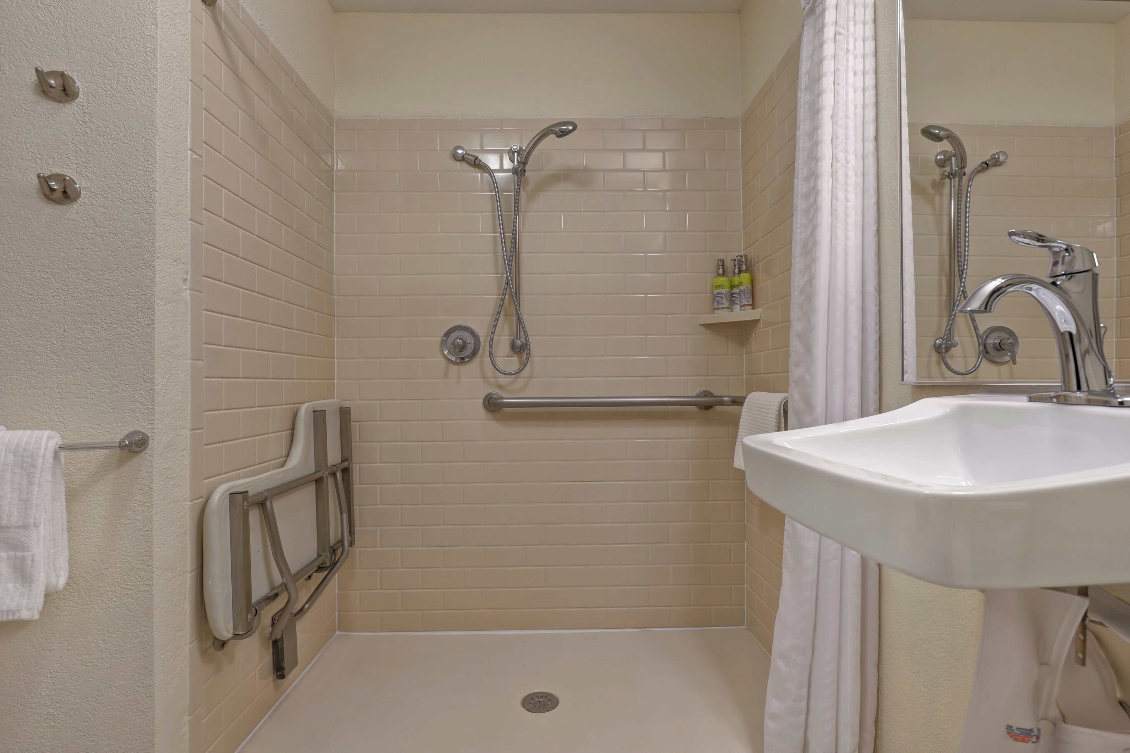 A bathroom with a white sink, a mirror, a shower with a grab bar, and a towel rack.