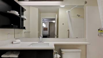 A modern bathroom with a white sink, a toilet, a shower, and a mirror reflecting the room.