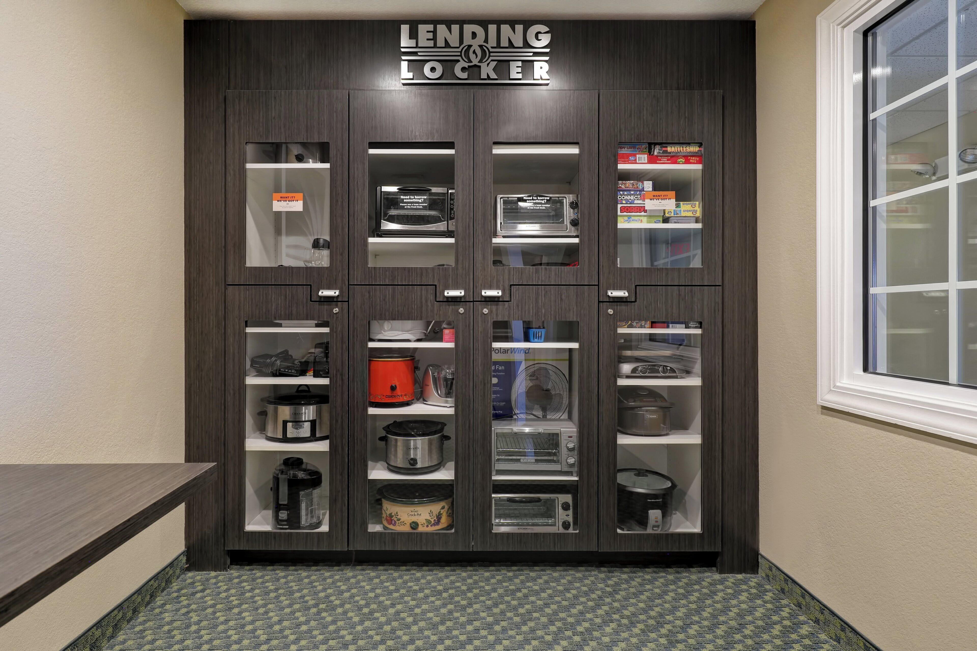 A kitchen with a 'LENDING LOCKER' sign, various appliances, and a window to the right.