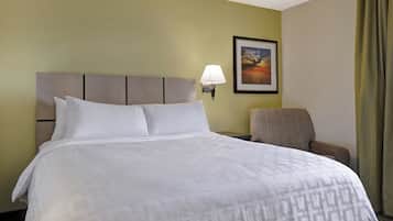 Quarto de hotel com cama grande, uma cadeira, luminária fixada na parede e uma moldura com imagem.