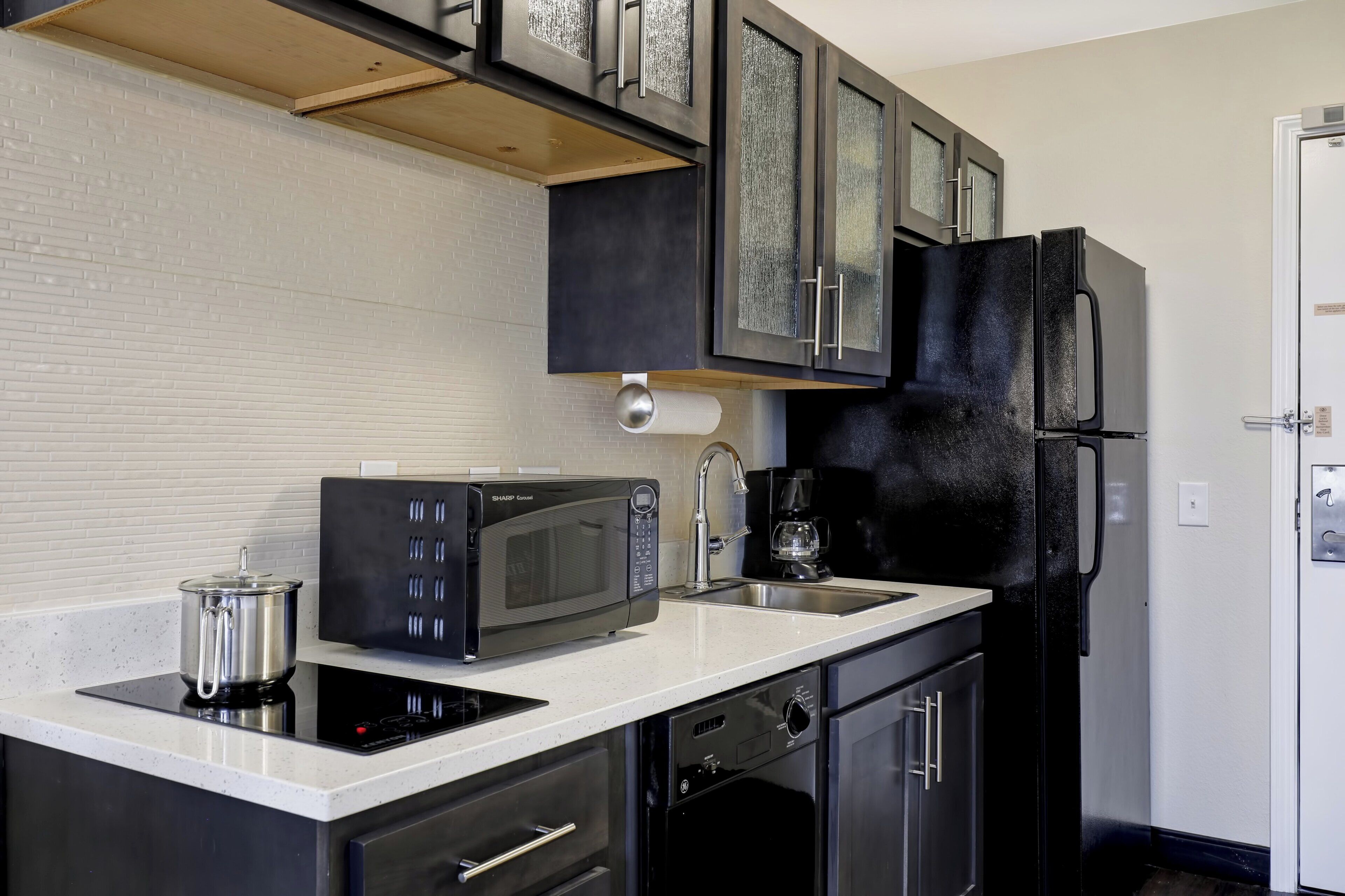 A modern kitchen with a built-in microwave, a coffee maker, and a black refrigerator.