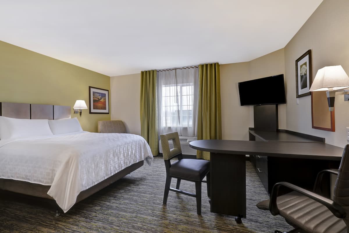 Une chambre d’hôtel avec un lit, un bureau, une chaise, une télévision et une fenêtre avec des rideaux.