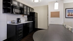 A compact kitchen with a microwave, refrigerator, and coffee maker. There is a dining table with chairs and a light fixture above. - Candlewood Suites Indianapolis - South by IHG (Greenwood)