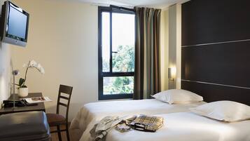 Una habitación de hotel con cama, escritorio con lámpara, silla, maleta y ventana con cortinas.