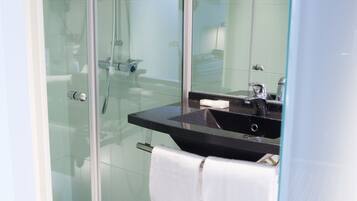 Un baño moderno con cabina de ducha de vidrio, un lavabo negro y una toalla blanca colgada en la puerta.