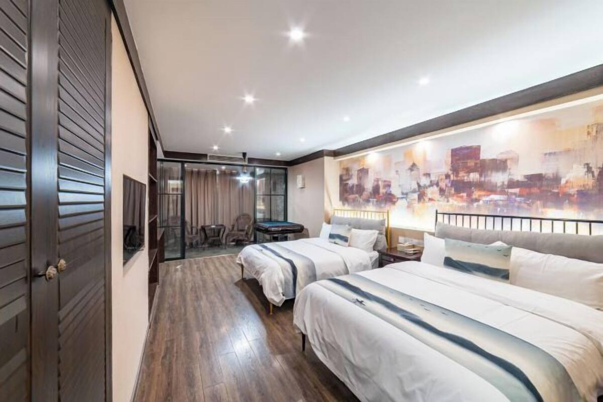 A hotel room with two beds, a pool table, a chair, and a large abstract painting on the wall.