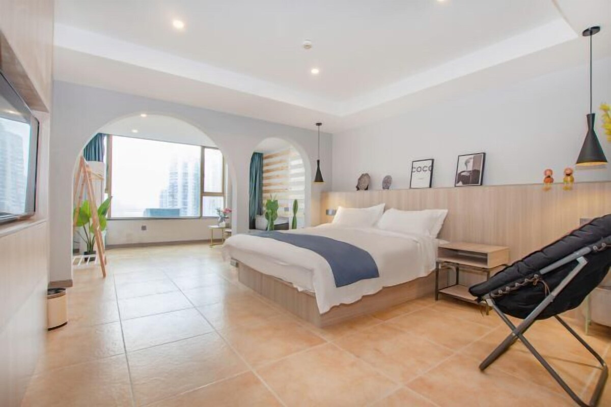 Habitación de hotel moderna con una cama grande, un escritorio y una silla. Se ve un ventanal con vistas a edificios.