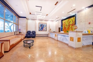 Un vestíbulo de hotel con recepción, área de descanso y un ventanal grande.