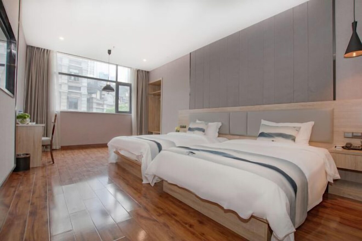 Un dormitorio moderno con dos camas, un ventanal grande y vistas a edificios.