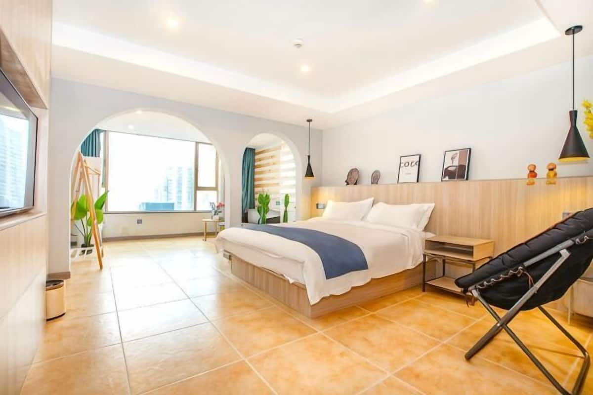 A modern hotel room with a large bed, a desk, a chair, and a view of the city.