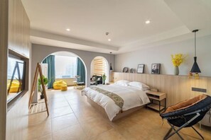 Un dormitorio moderno con una cama grande, una zona de estar con un sillón amarillo y vistas a la ciudad a través de amplios ventanales.