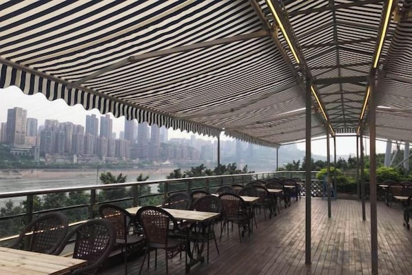Terraza al aire libre con mesas y sillas, con vistas a un río y al horizonte de la ciudad.