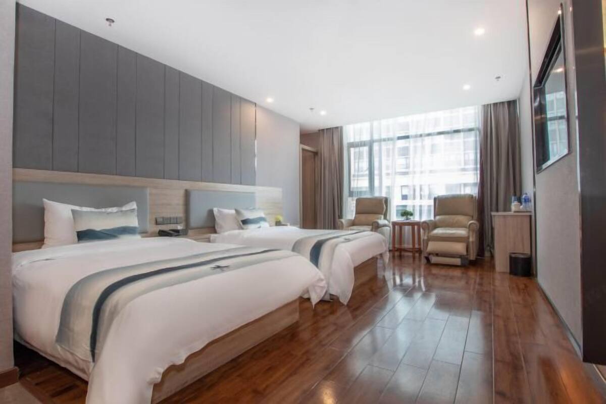 A hotel room with a large bed, two chairs, a small table, and a large window.