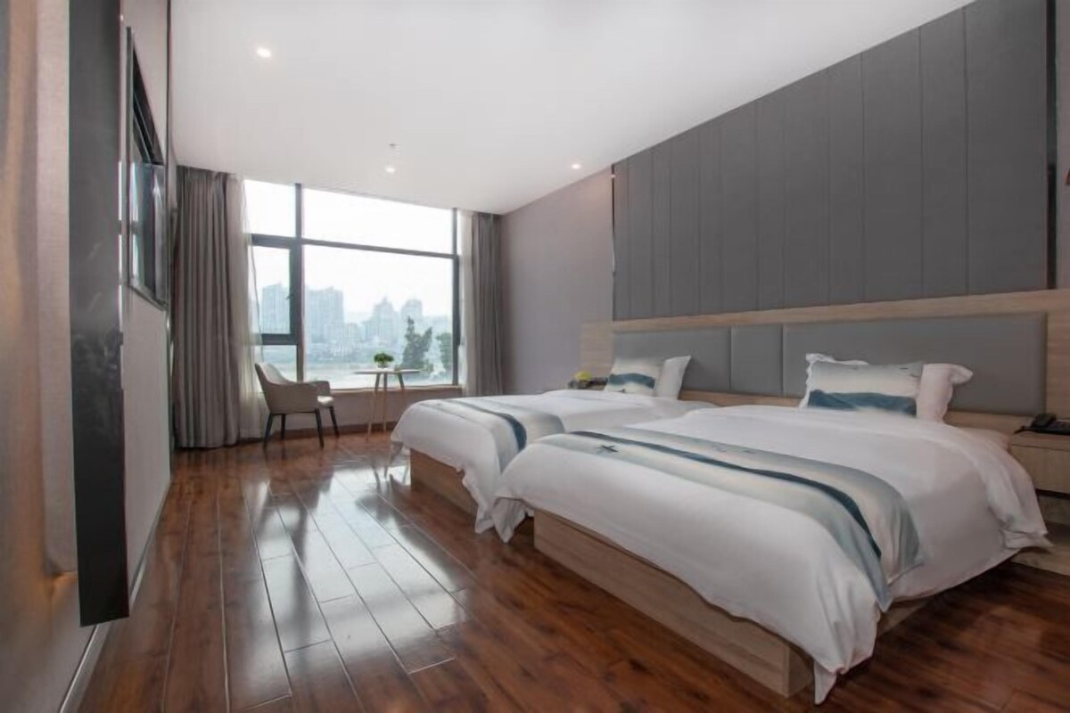 Una habitación de hotel moderna con dos camas, un ventanal grande y vistas a la ciudad.