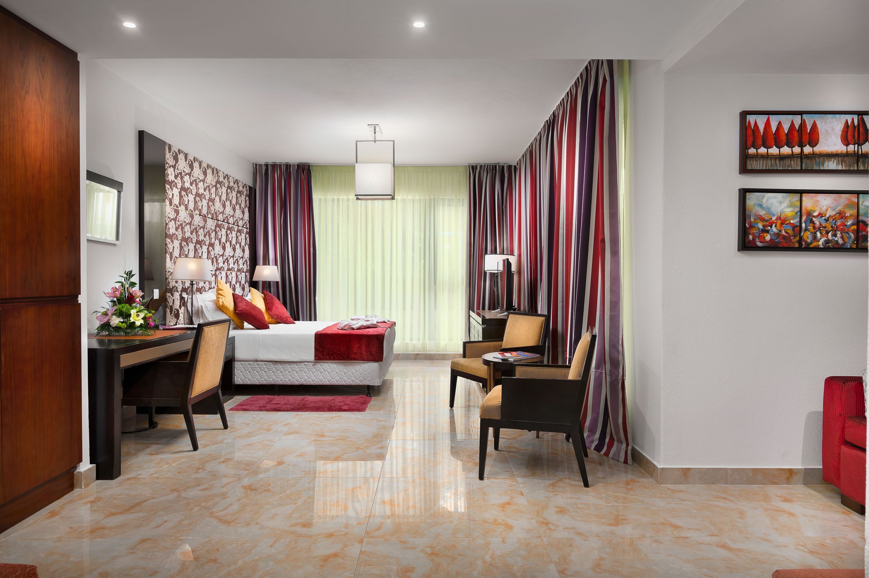 Une chambre d’hôtel avec un lit, un bureau, des chaises et des œuvres d’art accrochées aux murs.