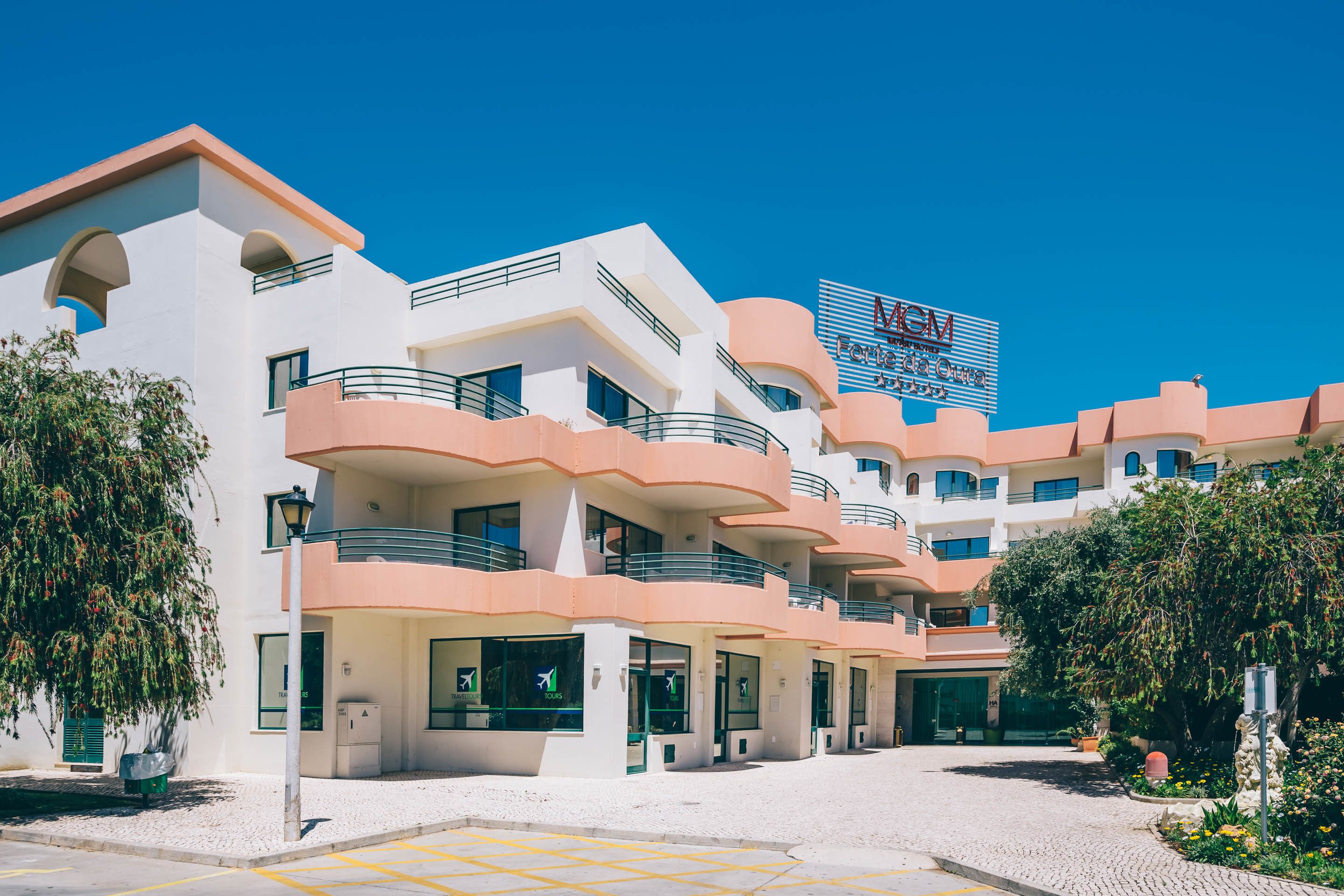 Un hotel de varios pisos con balcones, cielo despejado y un cartel.