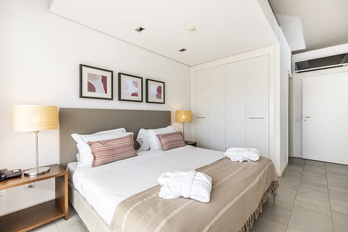 A hotel room with a bed, bedside lamps, a nightstand, a wardrobe, and framed artwork on the wall.