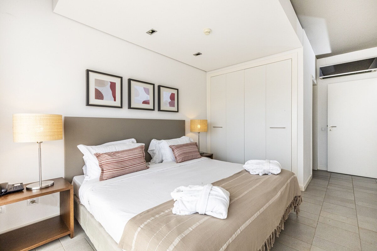 A hotel room with a bed, bedside lamps, a nightstand, a wardrobe, and framed artwork on the wall.
