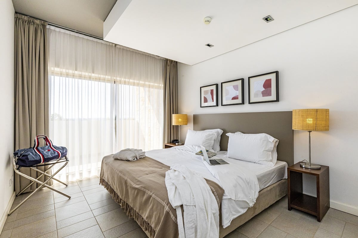 A hotel room with a bed, a desk, a lamp, a chair, and a window with curtains.