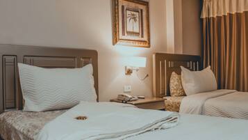 A hotel room with two beds, a nightstand with a lamp, a framed picture on the wall, and a window with curtains.