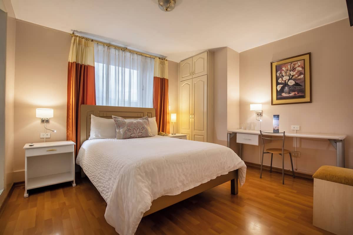 A bedroom with a bed, bedside tables, a desk, and a chair.