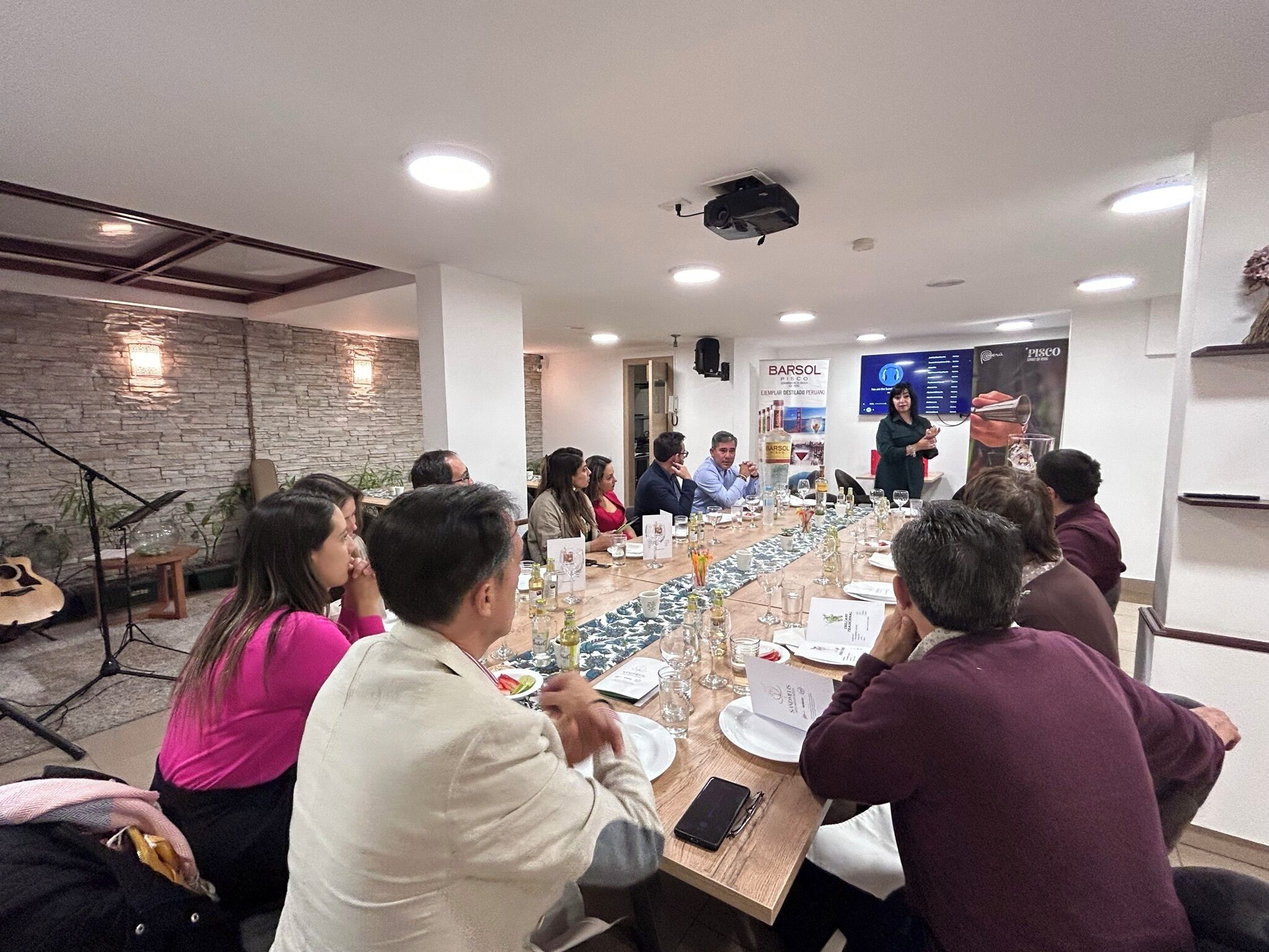 A conference room with a long table, several people seated, and a presentation screen in the background.