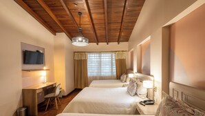 A hotel room with two beds, a desk with a chair, a TV mounted on the wall, and a window with curtains. - Sandmelis (Quito)