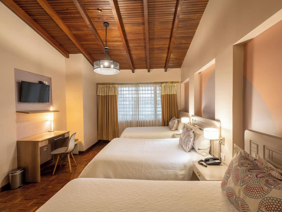 A hotel room with two beds, a desk with a chair, a TV mounted on the wall, and a window with curtains.
