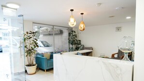 A modern reception area with a marble counter, potted plants, a blue sofa, and hanging pendant lights. - Sandmelis (Quito)