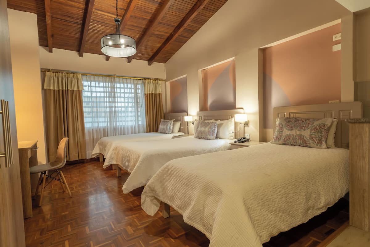 A hotel room with two beds, wooden flooring, a desk, and a chair.