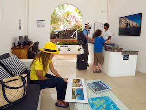 A hotel reception area with a desk, a waiting area with a sofa, and a view of a natural landscape through an archway. - Hotel Albemarle Galapagos Beachfront (Puerto Villamil)