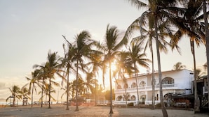 Una playa con palmeras y un edificio blanco con ventanas arqueadas.