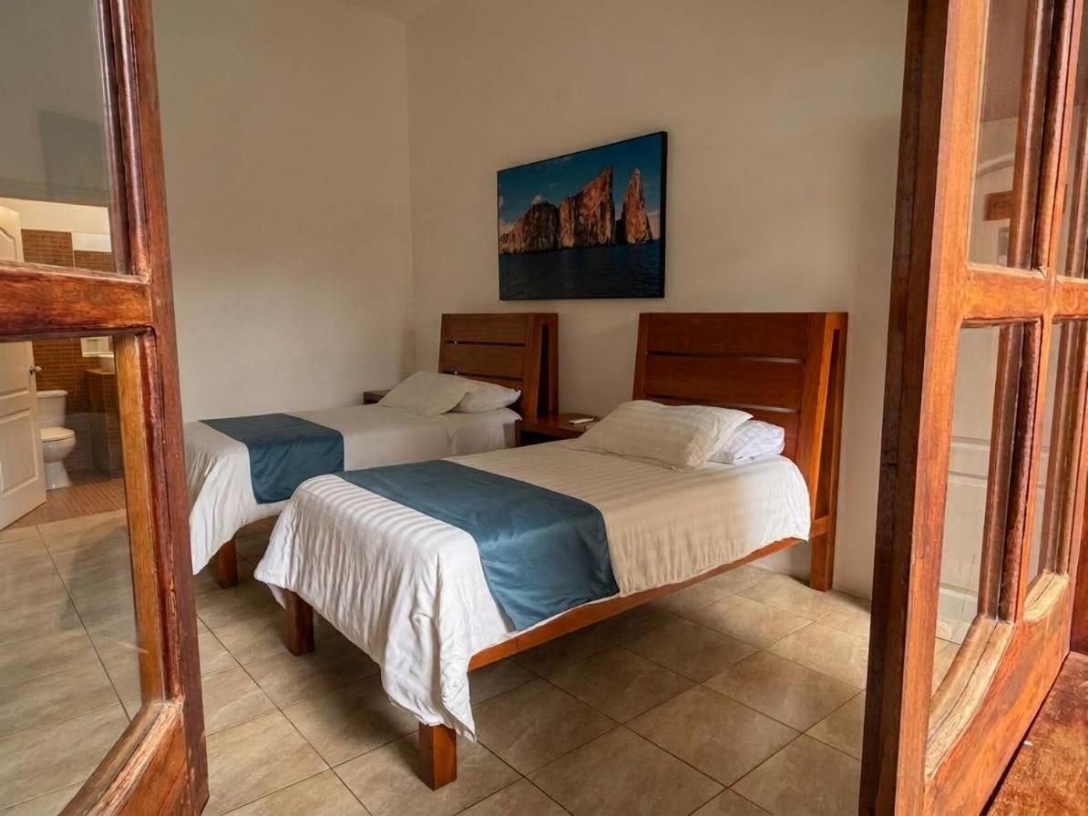 A hotel room with two beds, a painting on the wall, and a wooden door frame.