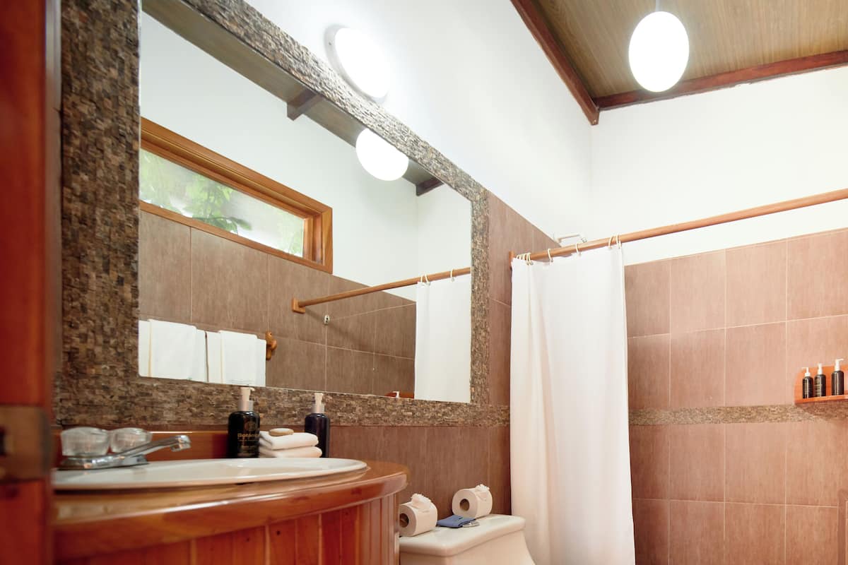 A bathroom with a wooden vanity, a large mirror, a shower with a curtain, and toiletries on the wall.