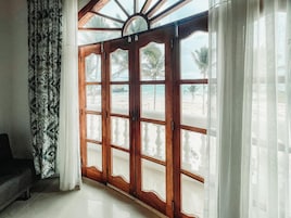 Habitación con una puerta de madera grande que da a vista de playa, un cortinaje estampado y un sofá.