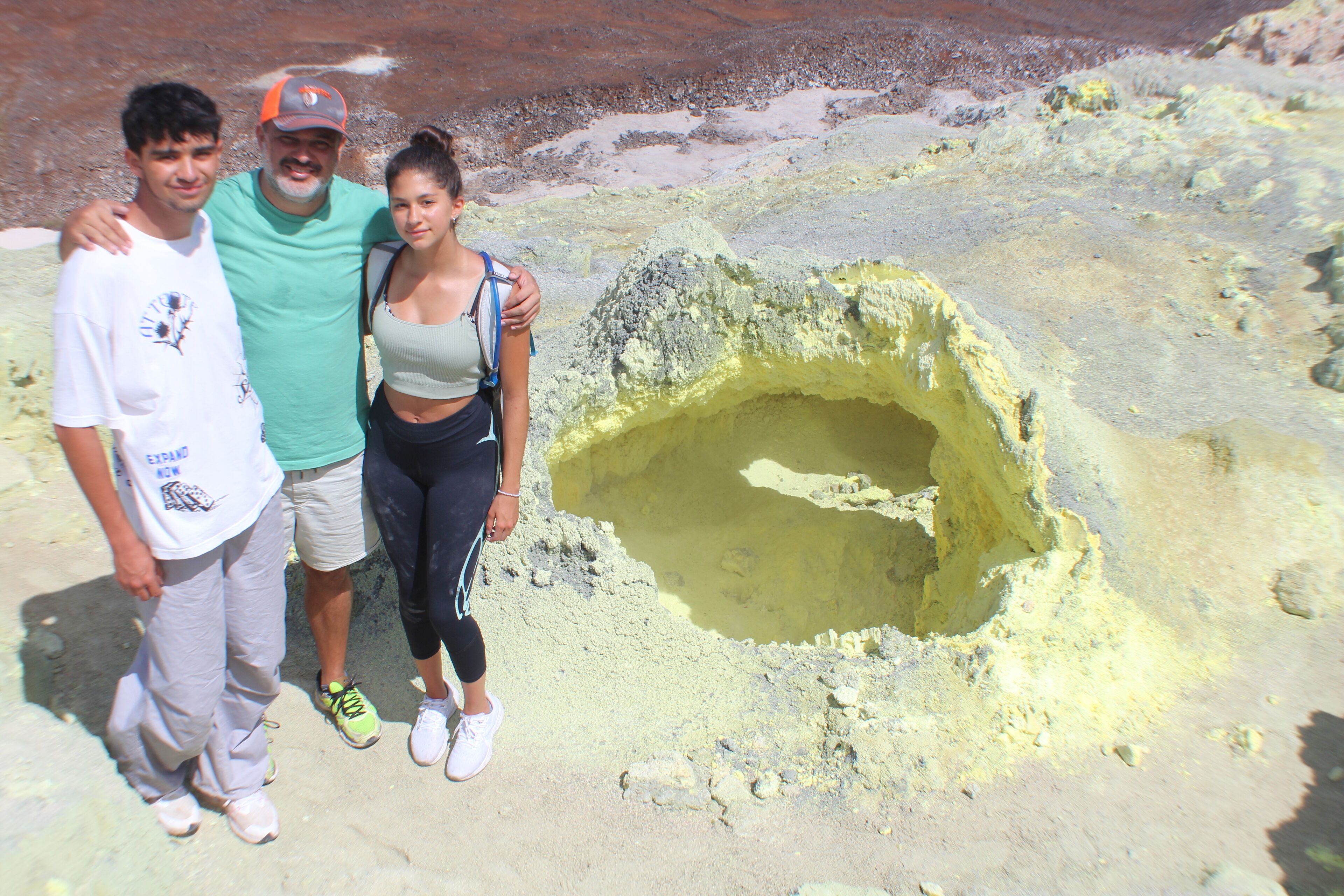 Three people standing near a geological formation with a large hole.