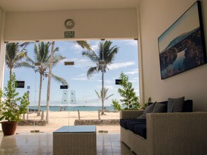A room with a view of a beach, a wicker sofa, a clock, and a painting.