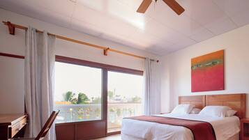 Habitación de hotel con cama, escritorio, silla, balcón con vistas y ventilador de techo.
