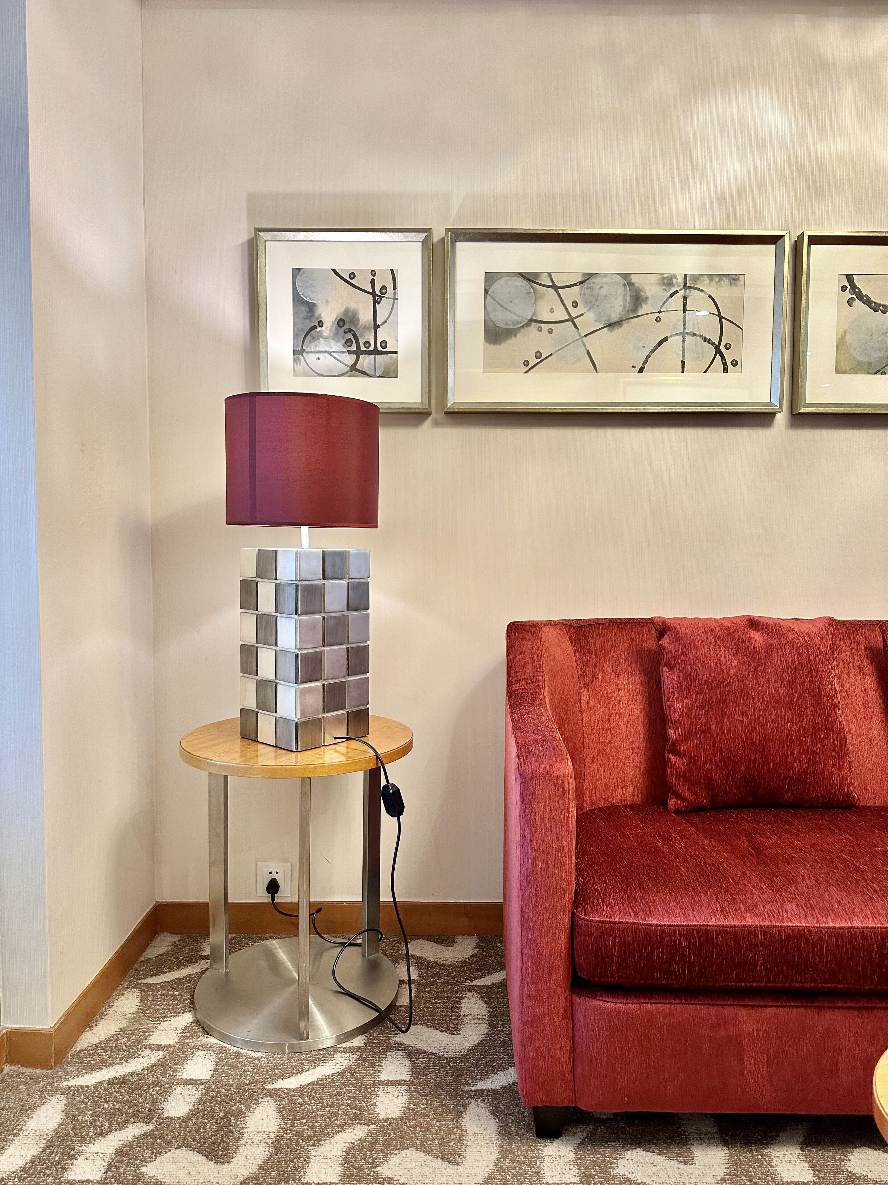 Una sala de estar con un sofá rojo, una lámpara con base a cuadros y tres cuadros abstractos en la pared.
